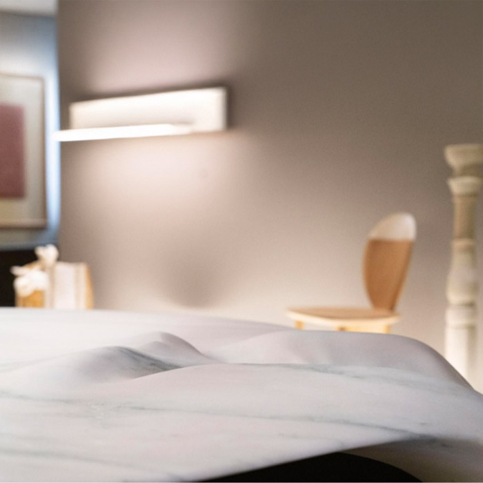 Detail of sculptural marble tabletop by OnEntropy with soft surface undulations, set in a contemporary interior with wooden chair and ambient lighting