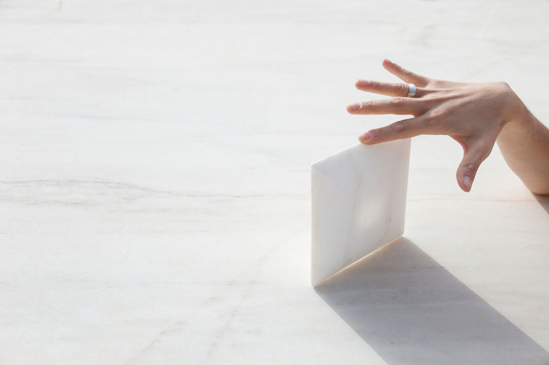 Hand interacting with a thin upright white marble slab on a smooth stone surface, highlighting material purity, balance, and OnEntropy’s tactile approach to design.
