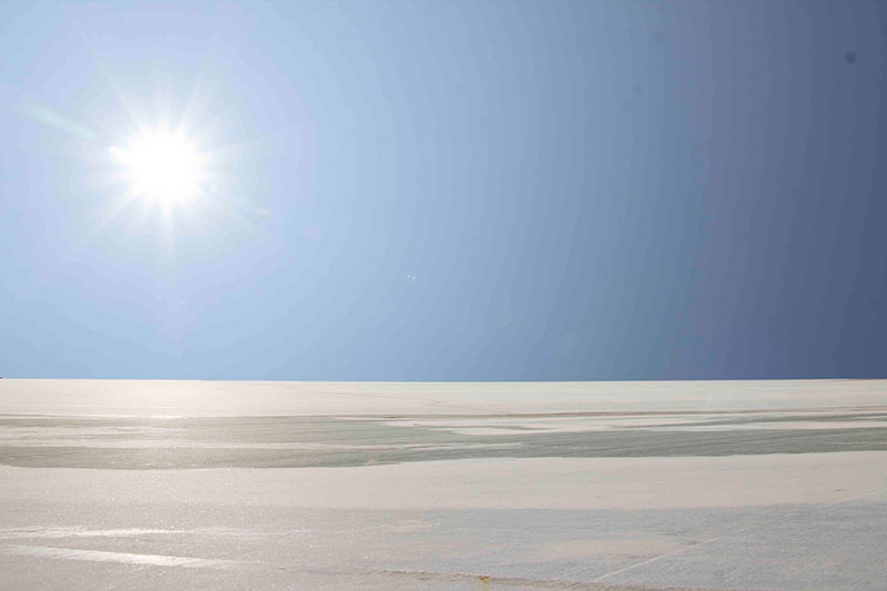 Bright midday sun over a smooth marble quarry landscape with a clear blue sky, capturing light, texture, and natural stone surface reflections