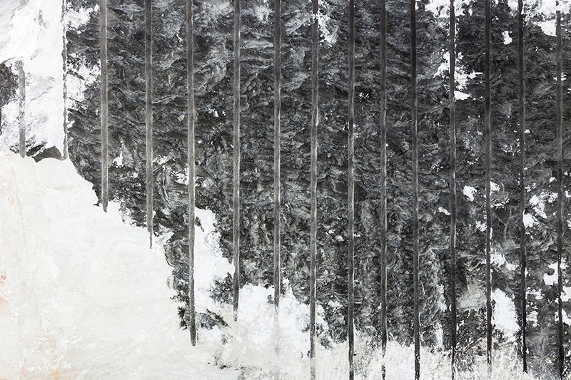 Close-up of marble quarry wall with vertical saw marks and contrasting black and white stone textures, revealing raw extraction process and geological layers.