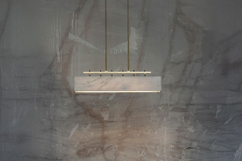 Suspended marble pendant light by OnEntropy with brass hardware, installed against a veined quarry wall, showcasing elegant material contrast and artisanal lighting design.