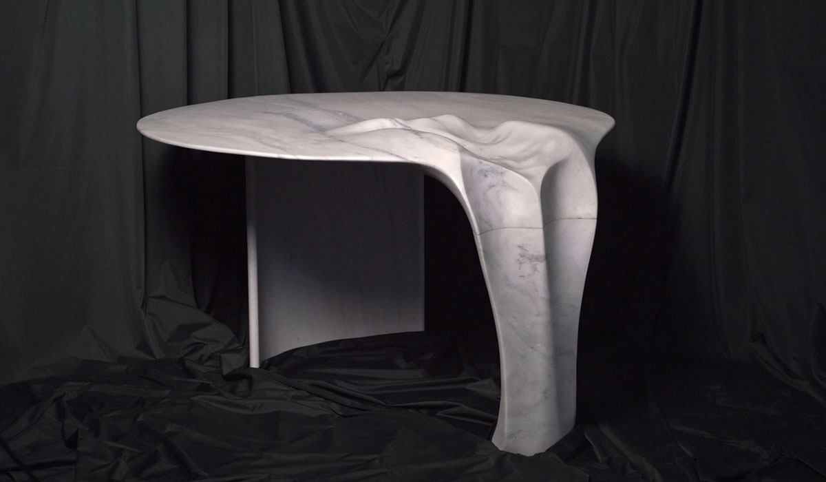 Sculptural white marble table by OnEntropy featuring organic, fluid forms and asymmetric structure, showcased against a dark draped background.