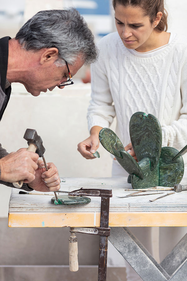 Two artisans working on a green marble sculpture, using chisels and hammers at a workshop table—demonstrating OnEntropy’s collaborative and hands-on approach to marble craftsmanship.
