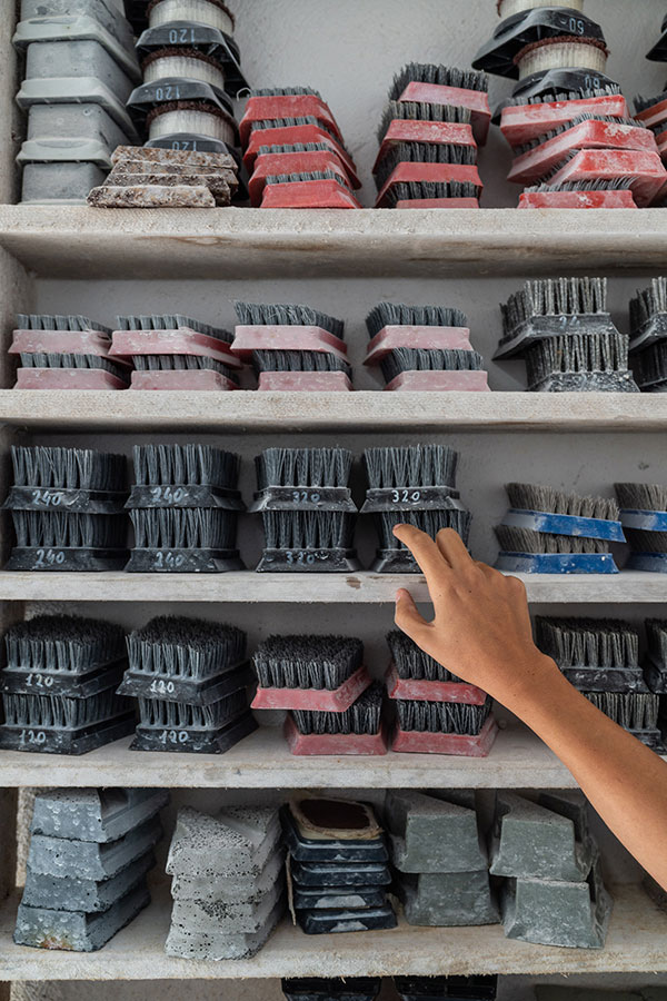 Hand reaching for a labeled abrasive brush among neatly organized polishing tools and stone samples on workshop shelves—illustrating the material precision in OnEntropy’s marble finishing process.