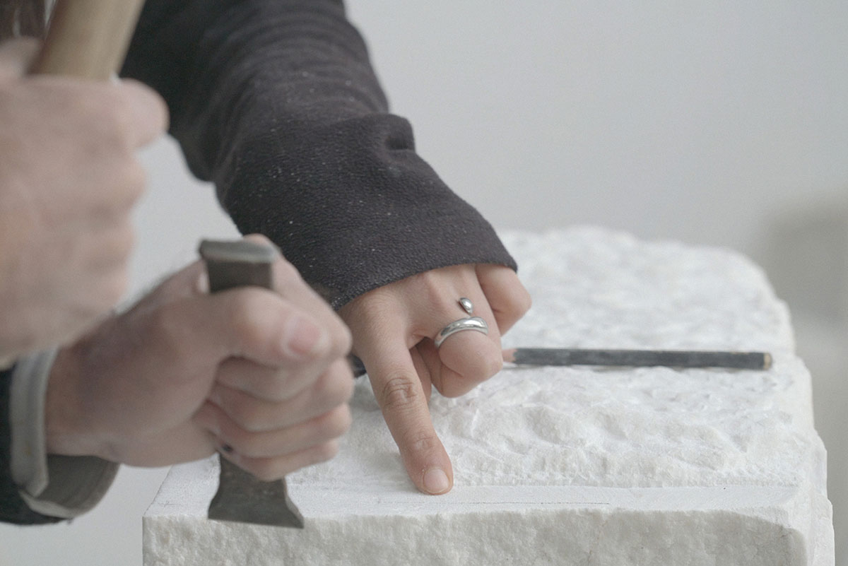 Close-up of hands marking and chiseling white marble, illustrating precision and collaboration in OnEntropy’s handcrafted stonework process.